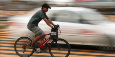 man biking along road with taxi in background